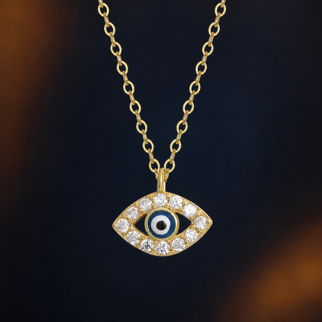 Gold-tone evil eye pendant necklace on a dark navy and warm amber Halloween editorial background
