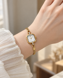 White-dial gold-tone GEDI octagonal quartz bracelet watch worn on an adult wrist with a cream blouse
