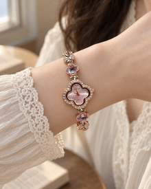Pink AIMANA clover bracelet watch worn on an adult wrist with a cream lace sleeve