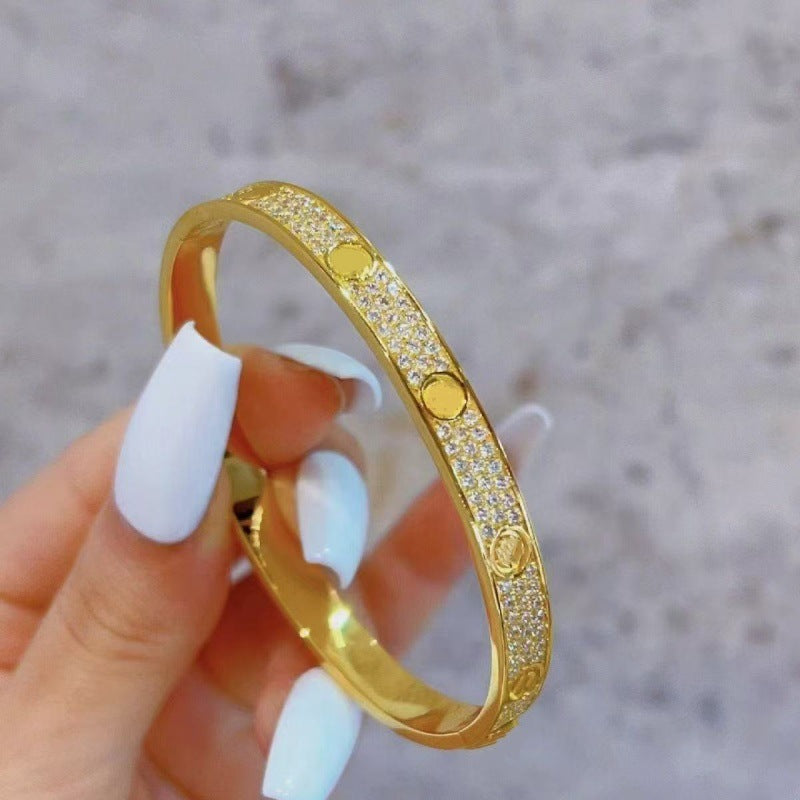 Gold tone cubic zirconia screw motif bangle held in hand