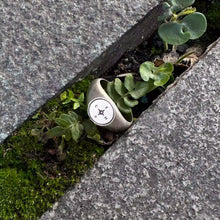 Vintage compass signet ring photographed among stone and greenery