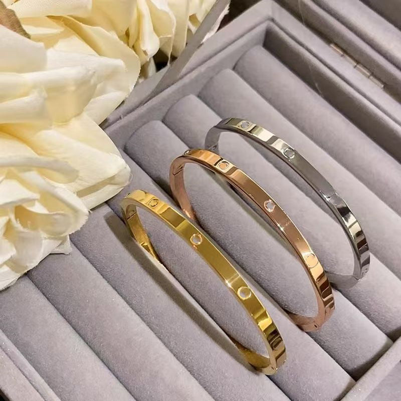 Gold, rose gold and silver tone plain screw motif hinged bangles in a jewelry tray