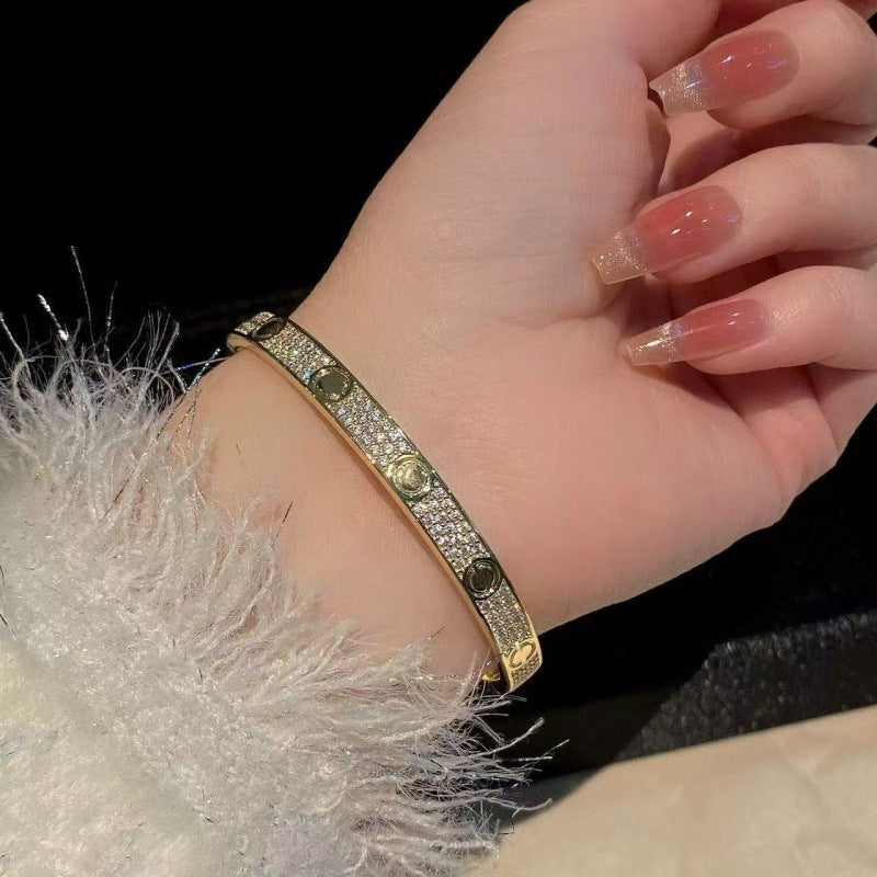 Gold tone three-row cubic zirconia screw motif bangle worn on wrist