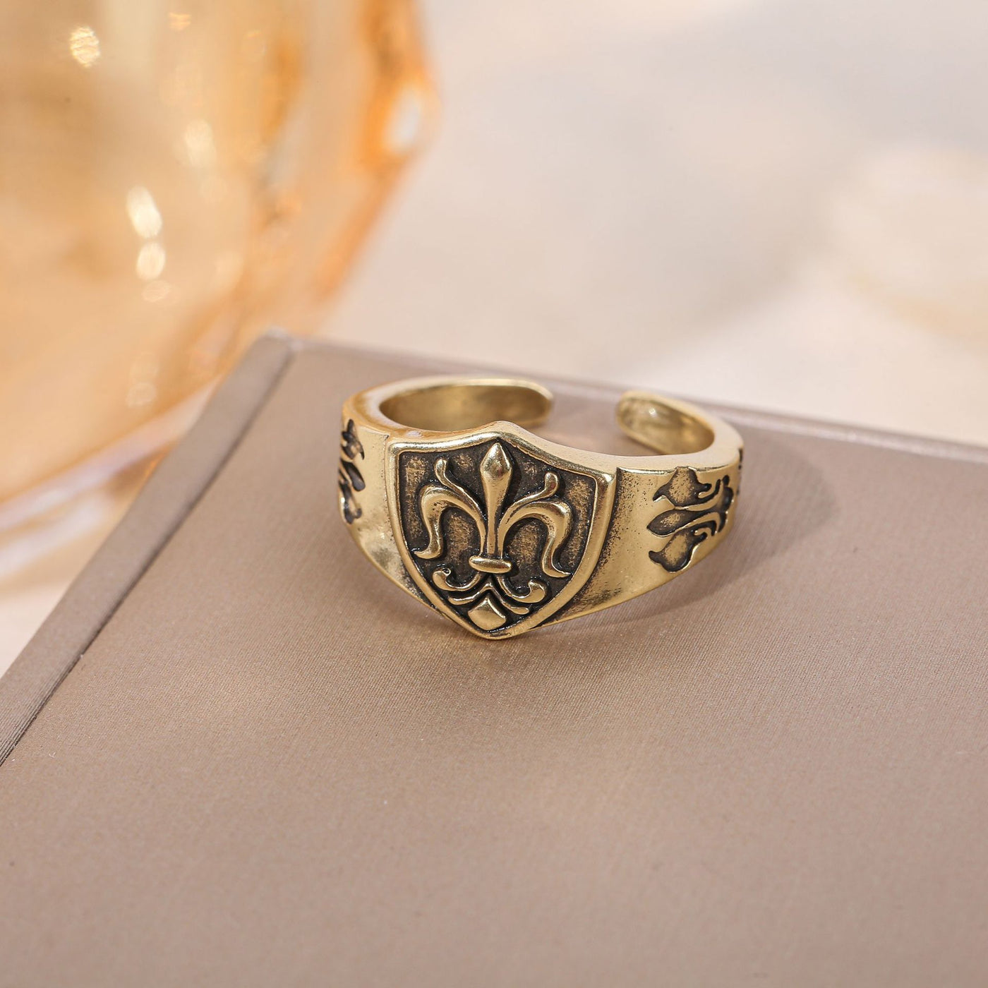 Antique Gold fleur-de-lis shield adjustable ring on a neutral display