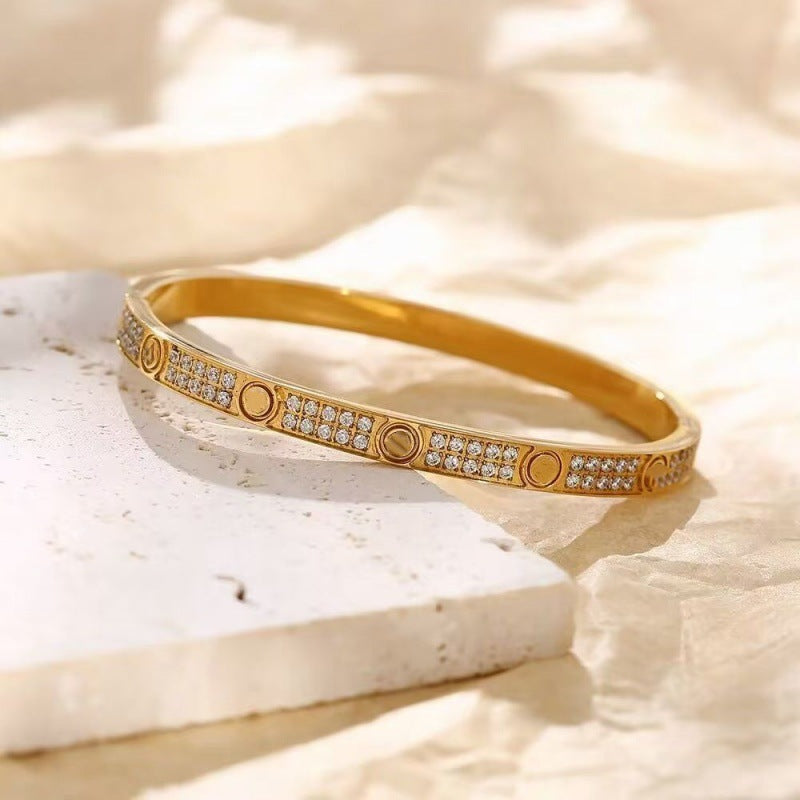 Gold tone two-row cubic zirconia screw motif bangle in warm light