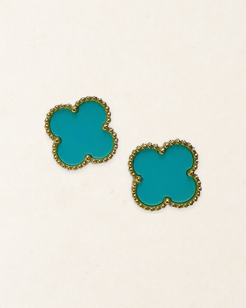 Pair of Aqua Blue four-leaf clover stud earrings with gold-tone beaded borders on a pale paper-texture background.