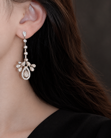 Four-link CZ chandelier earring with crown and teardrop detail beside a black dress neckline