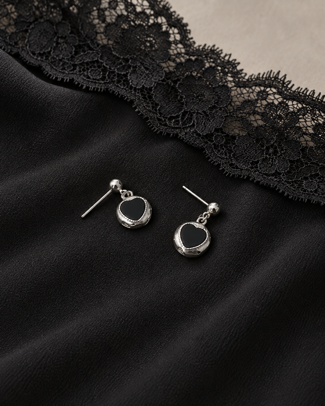 Silver-tone black heart drop earrings on black dress fabric beside a lace edge