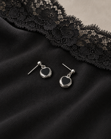 Silver-tone black heart drop earrings on black dress fabric beside a lace edge