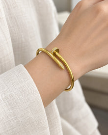 Gold-tone nail bangle with clear stone accents worn around an adult wrist