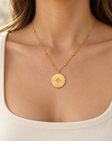 Gold-tone compass medallion necklace with station beads worn at an adult neckline