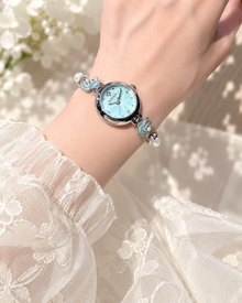 Blue camellia flower and pearl-look bracelet watch worn with an ivory blouse